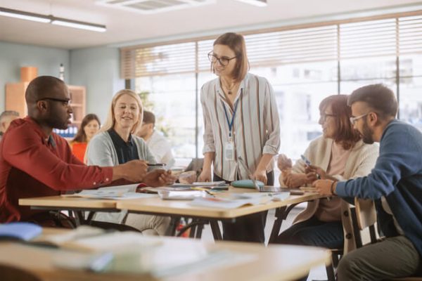 Adult Education Center: Adult Students Learning in Classroom, Working as Two Teams on a Verbal Education Game. Positive Female Teacher Giving Advice, Answering Questions, and Motivating Students